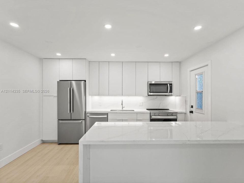 Kitchen featuring flat-panel cabinetry, a waterfall-edge stone island, stainless steel appliances, recessed ceiling lighting, and wood-finish flooring