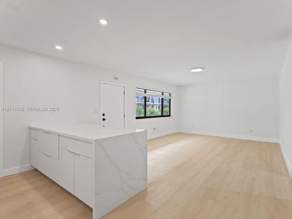 Open-concept interior featuring light wood-finish flooring, white cabinetry with a waterfall edge stone countertop, and recessed lighting
