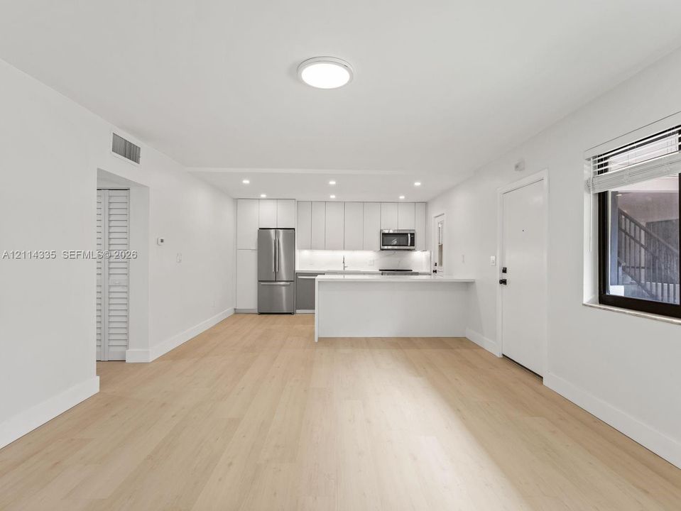 Open-concept area featuring light wood-finish flooring, white flat-panel cabinetry, a stainless steel refrigerator, a built-in microwave, and a white breakfast bar