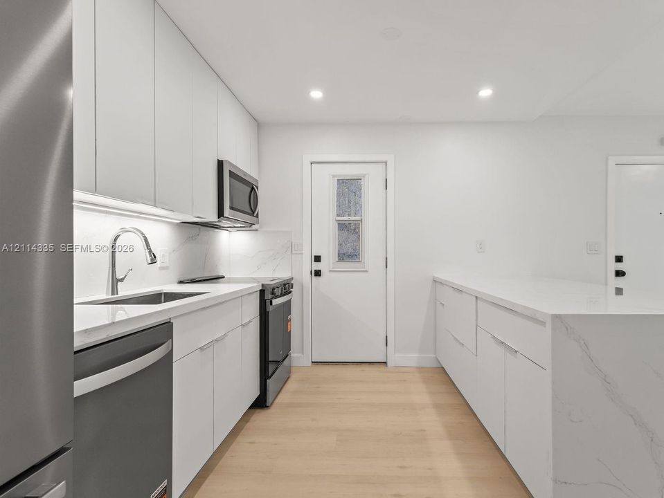 Kitchen featuring flat-panel cabinetry, light-toned stone-finish countertops, stainless steel appliances, and wood-finish flooring