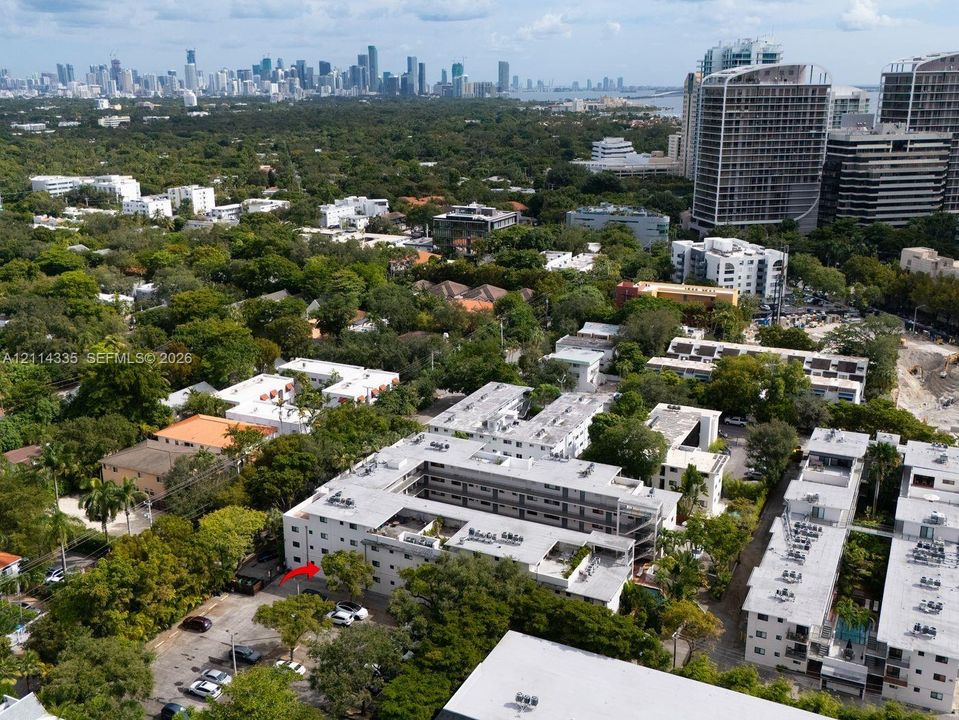 Aerial perspective of mid-rise multi-unit residential building featuring a courtyard layout, flat roof construction, exterior surface parking, and dense mature landscaping