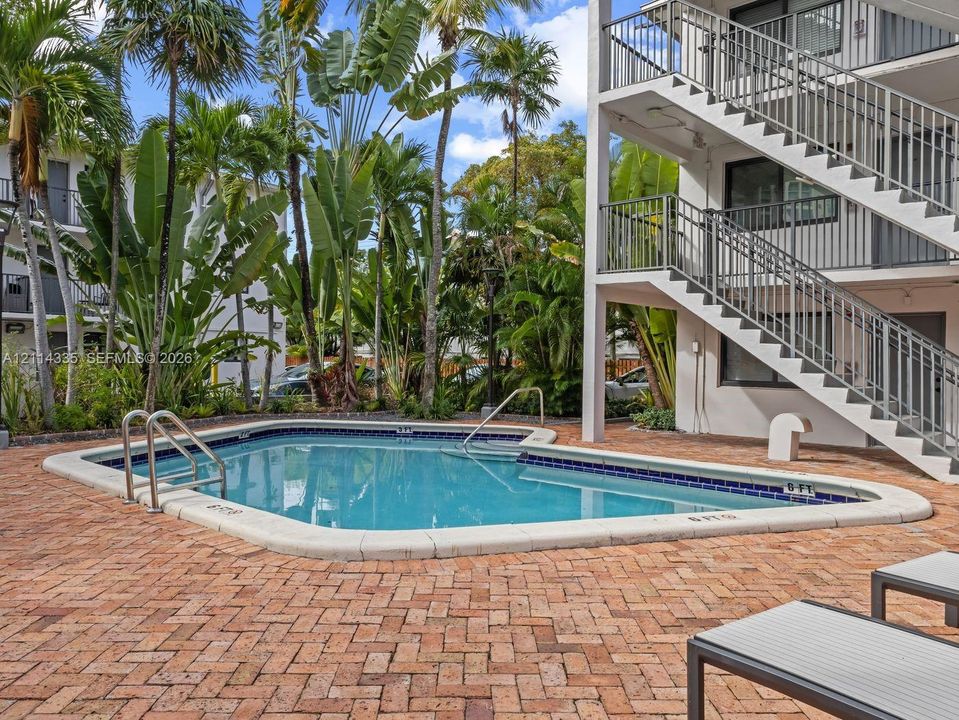 In-ground swimming pool with a tiled perimeter, expansive brick-paver deck, and surrounding mature palm trees