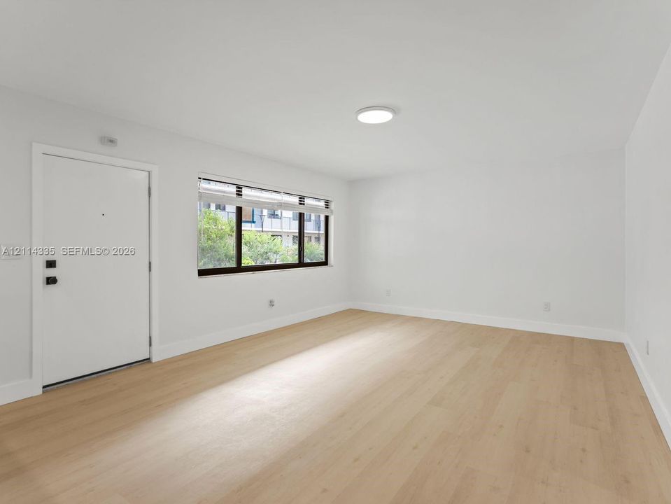 Neutral-toned space featuring wood-finish flooring, a flush-mount ceiling light, a white entry door with matte black hardware, and a window with a dark frame