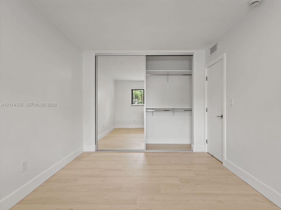Room featuring wood-finish flooring, sliding mirror closet doors, and built-in closet shelving