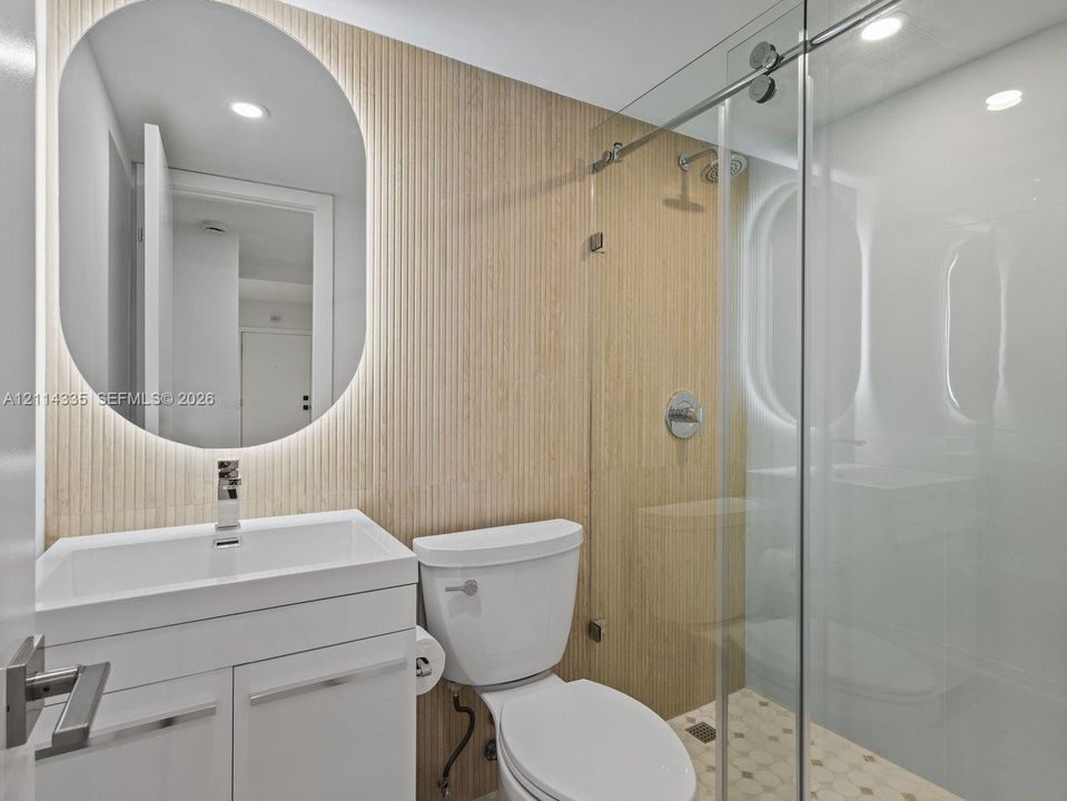 Bathroom featuring a white vanity, oval backlit mirror, vertical fluted wall paneling, and a glass-enclosed shower with mosaic floor tile