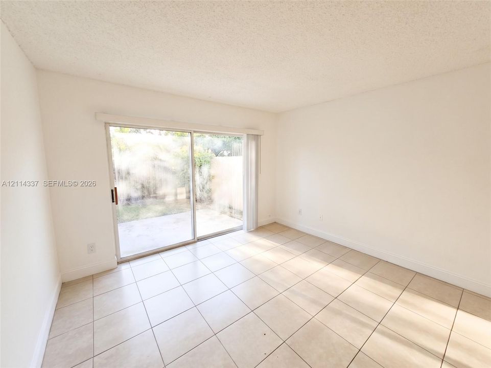 Interior space featuring neutral tile flooring, smooth-finish walls, and glass sliding doors leading to an exterior concrete patio