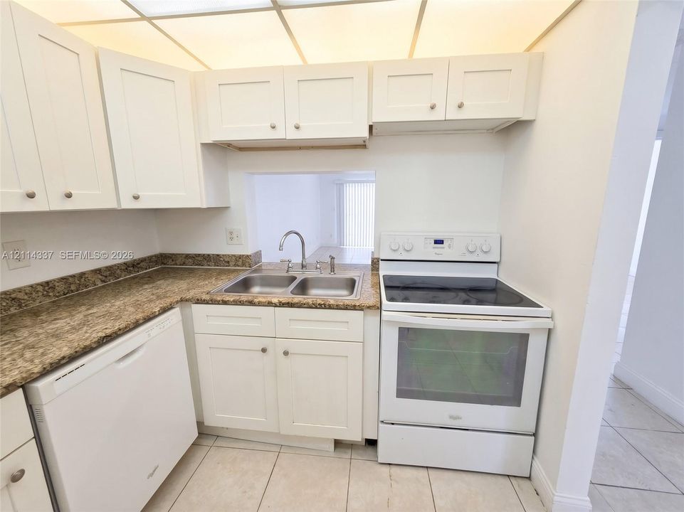 Kitchen featuring white cabinetry, stone-finish countertops, dual-basin stainless steel sink, tile flooring, and integrated white appliances