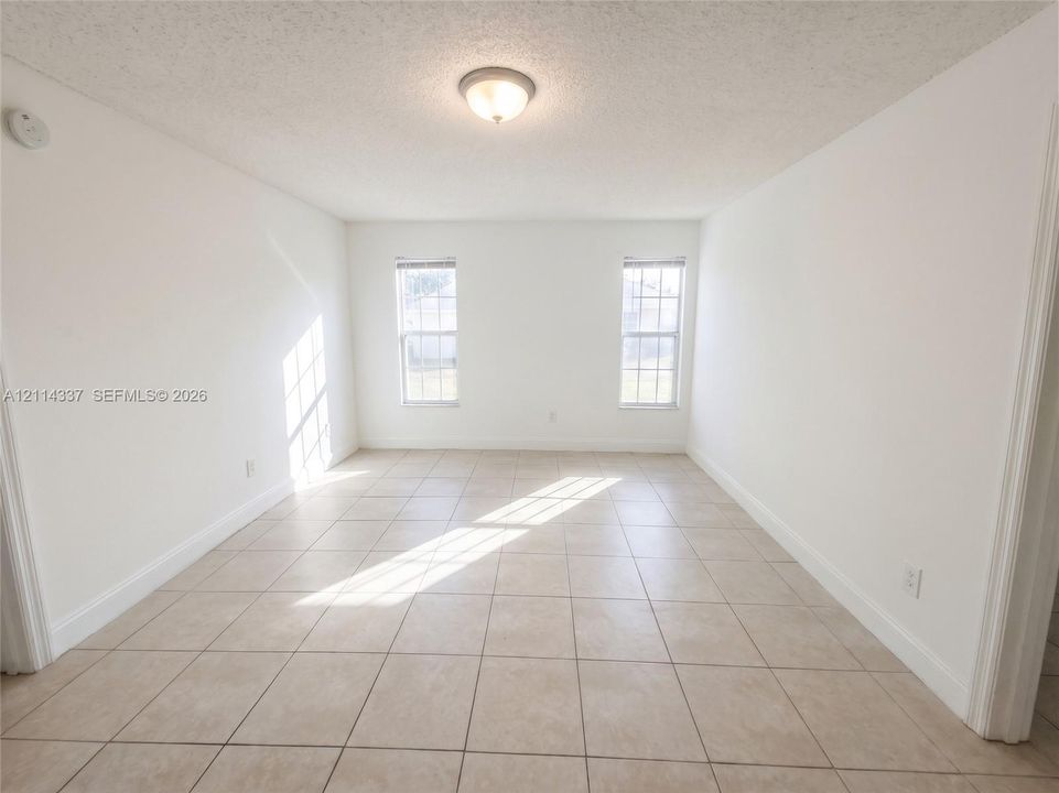 Neutral interior room featuring large-format ceramic tile flooring, two double-hung windows, and a flush-mount ceiling light fixture