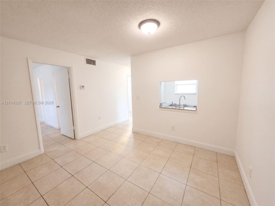 Neutral-toned ceramic tile flooring, interior pass-through window with solid-surface countertop, and flush-mount ceiling lighting
