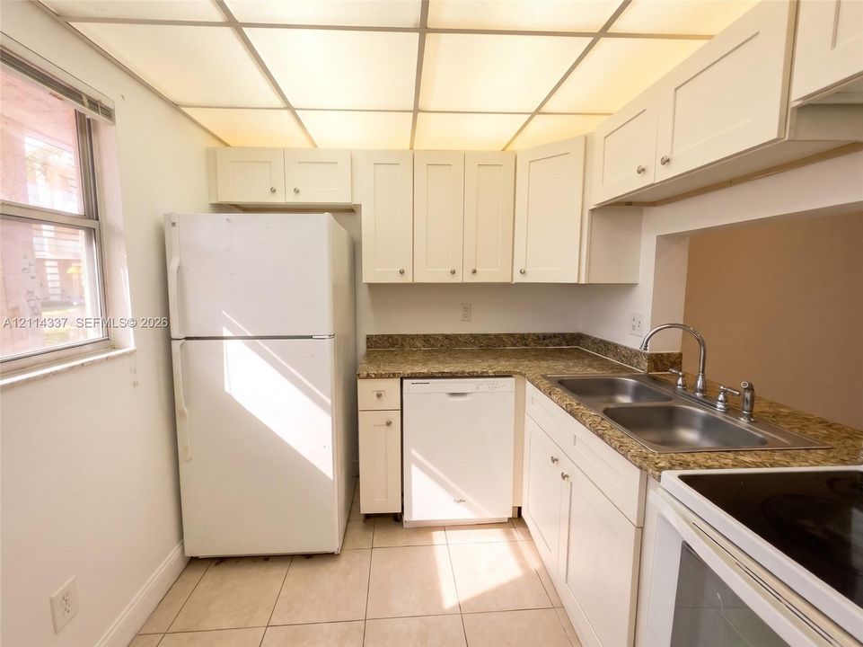 Kitchen featuring shaker-style cabinetry, stone-finish countertops, dual-basin stainless steel sink with pull-down faucet, integrated dishwasher, and tile flooring
