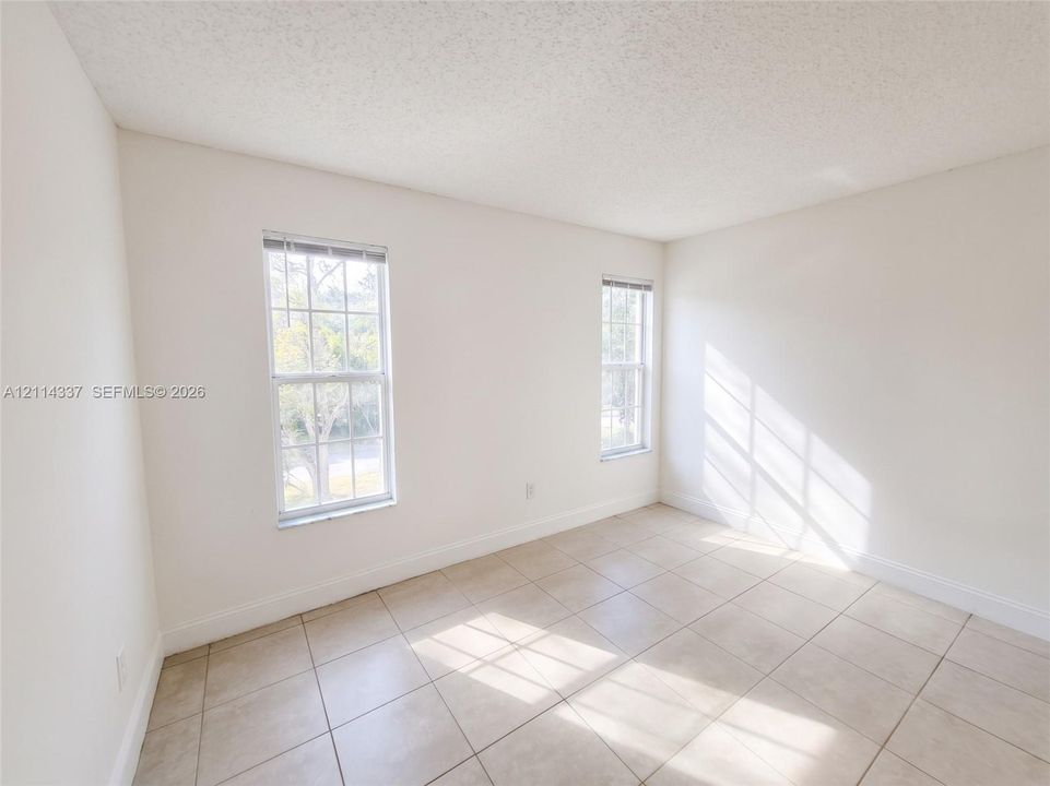 Interior room featuring large-format neutral tile flooring, white wall finishes, and two double-hung windows with integrated window treatments