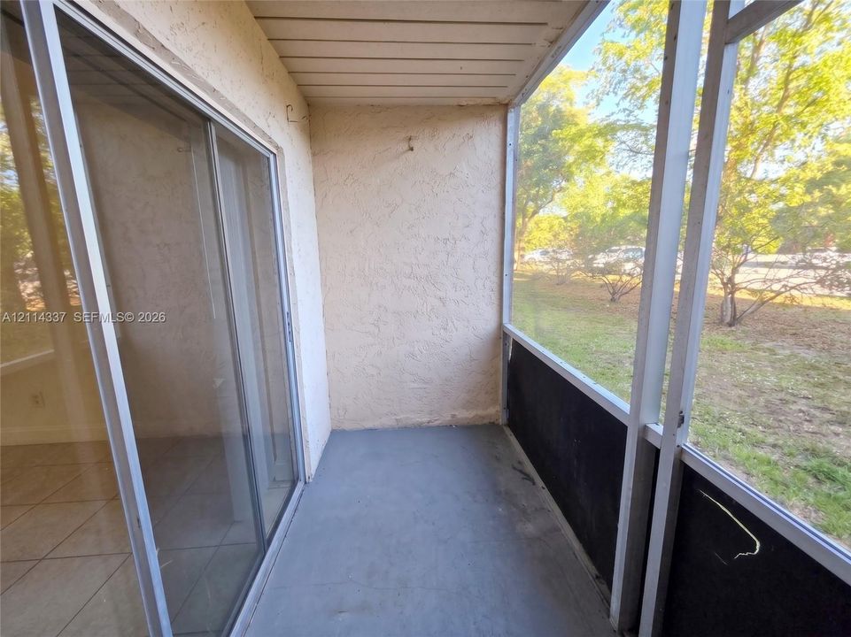 Screened-in balcony featuring a concrete floor, textured stucco walls, and sliding glass door entry