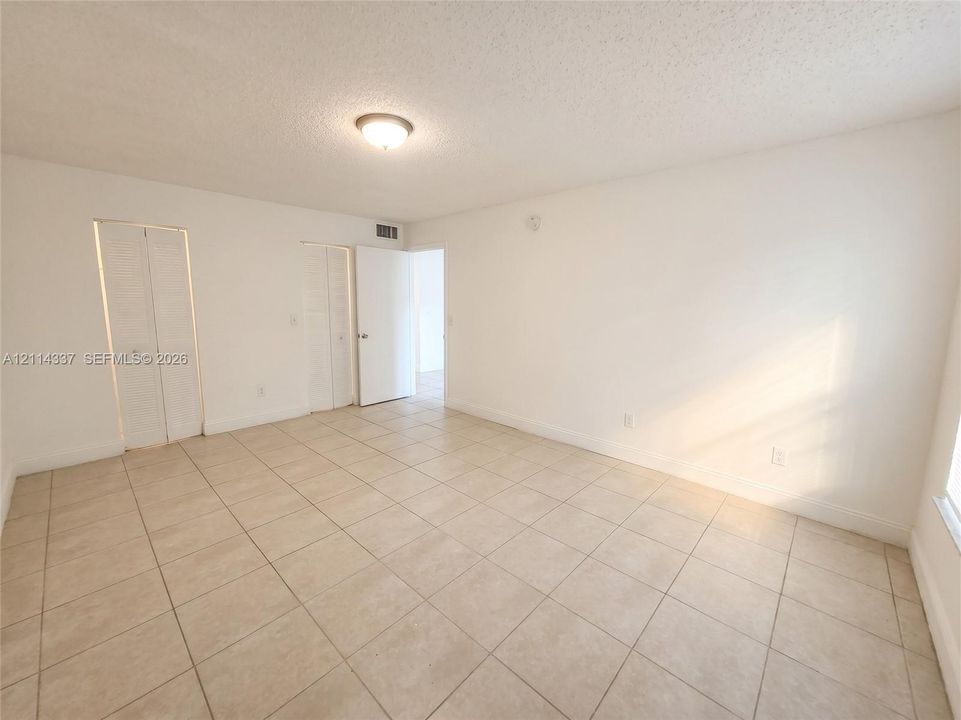 Neutral interior space featuring large-format ceramic tile flooring, dual bi-fold closet doors, and a flush-mount ceiling light fixture