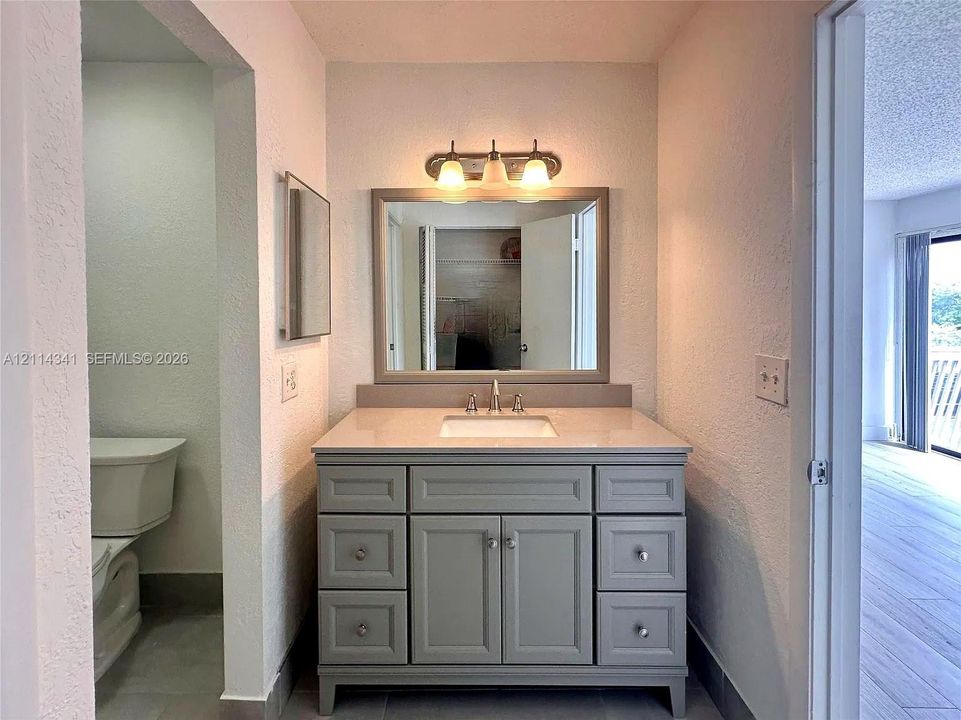 Bathroom vanity featuring a grey cabinet base, light-toned countertop, undermount sink, brushed-finish faucet, and a rectangular mirror with a coordinated frame, illuminated by a three-light fixture