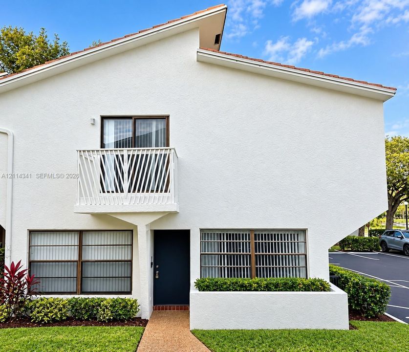 Stucco exterior featuring an asymmetric roofline, a second-story balcony with metal railing, and a built-in planter box