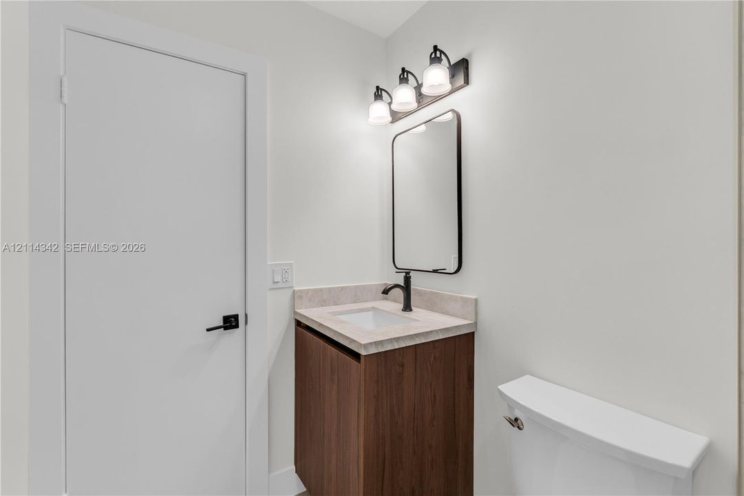 Bathroom featuring a wood-finish vanity with a stone-composite countertop, undermount sink, matte black faucet, and rounded-corner mirror with coordinating three-light fixture