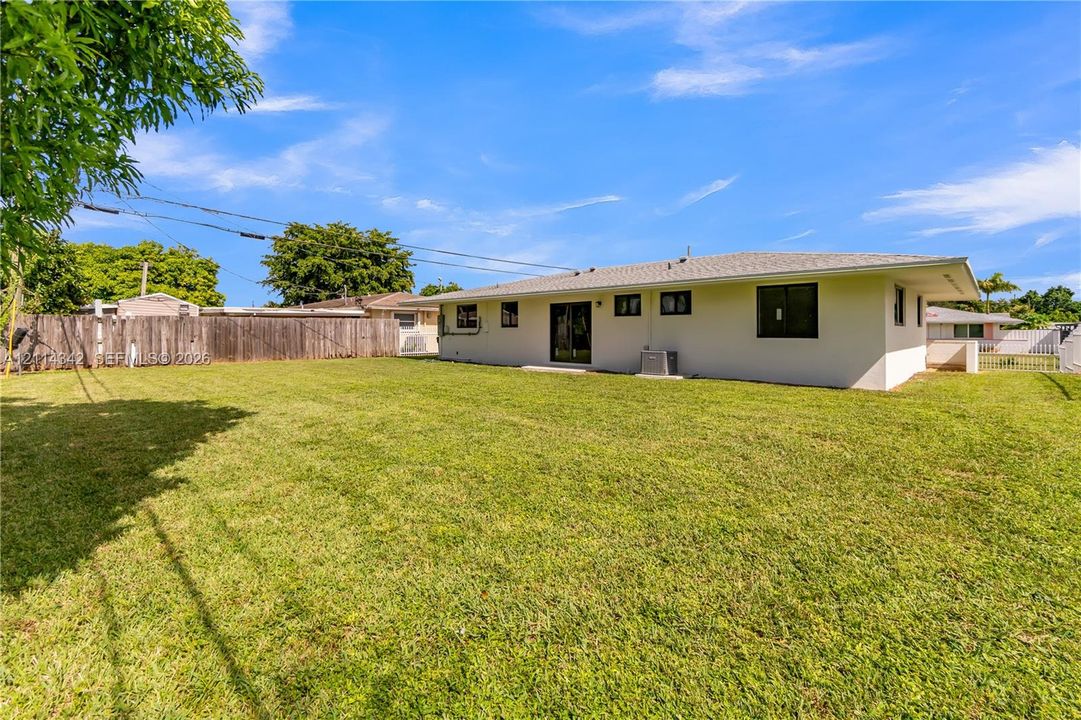 Expansive backyard featuring a large grass lawn, perimeter wood fencing, and exterior stucco siding