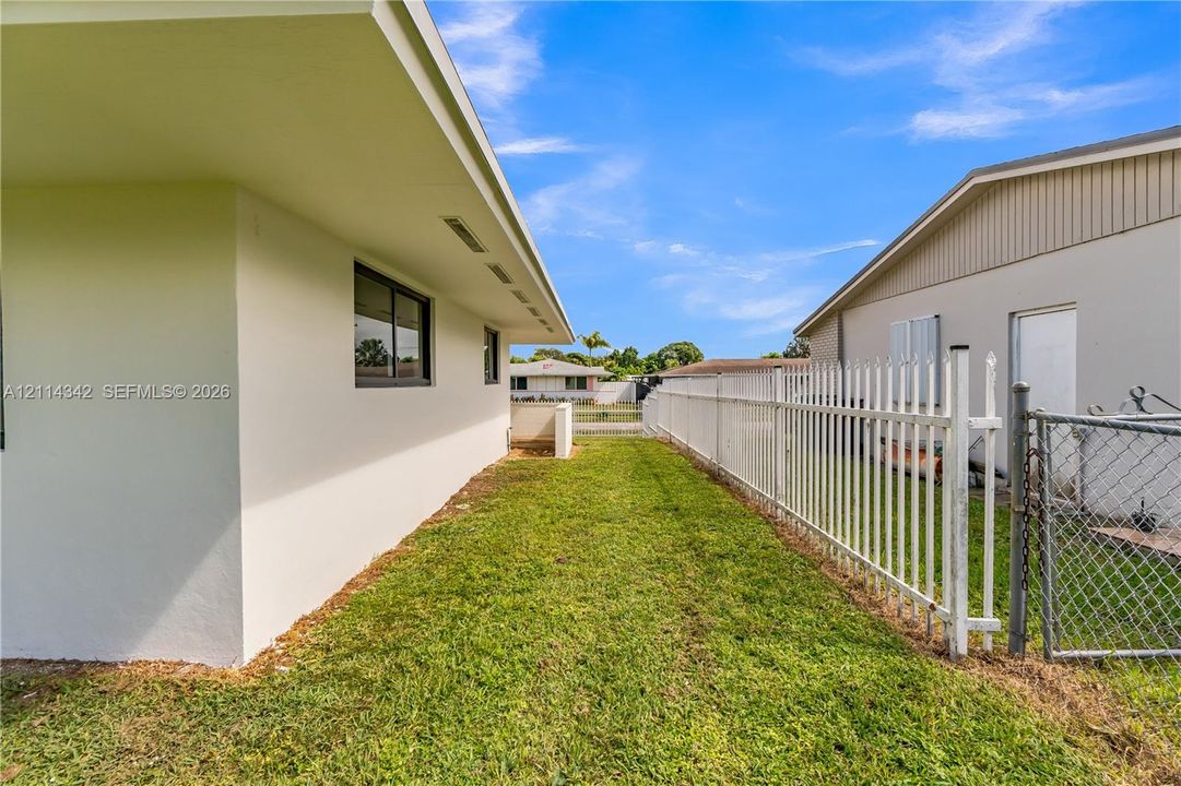 Exterior side yard featuring a grass lawn, white metal fencing, and a smooth stucco finish