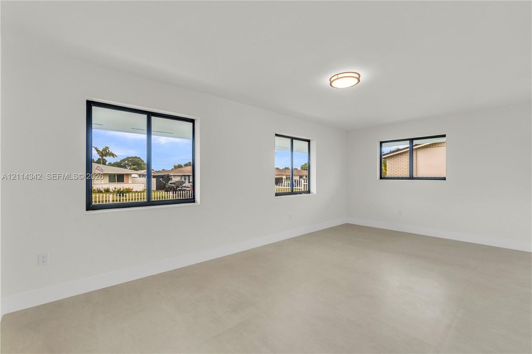 Neutral interior featuring light-toned tile flooring, minimalist white walls, black-framed sliding windows, and a flush-mount circular ceiling light fixture