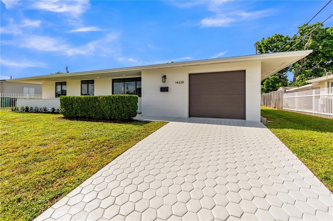Mid-century modern exterior featuring painted brick facade, overhanging eaves, an integrated one-car garage, and a geometric hexagonal paver driveway