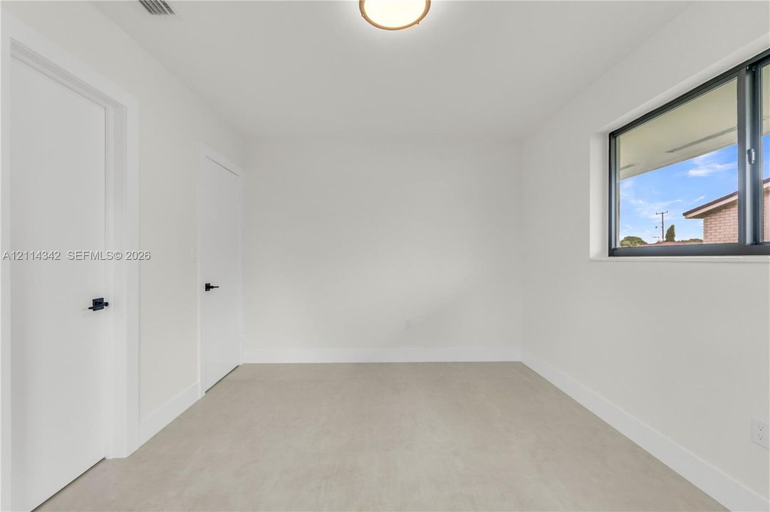 Bright interior featuring neutral-toned flooring, two doors with matte black hardware, a flush-mount ceiling light, and a window with a dark frame