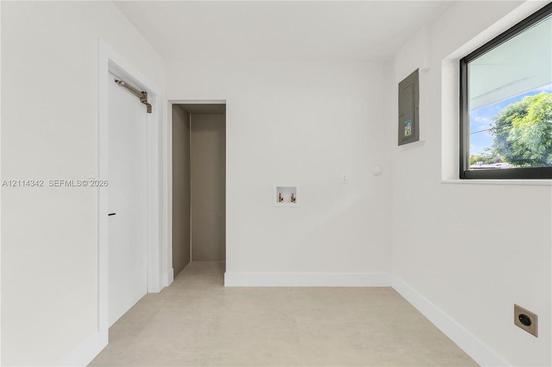Utility room featuring neutral tile flooring, a window with a black frame, recessed doorway, and dedicated water hookups