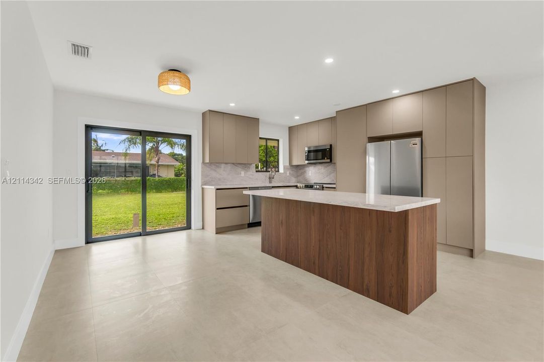 Kitchen featuring flat-panel cabinetry, a central island with wood-finish base, stone-surface countertops, stainless steel appliances, and glass sliding doors