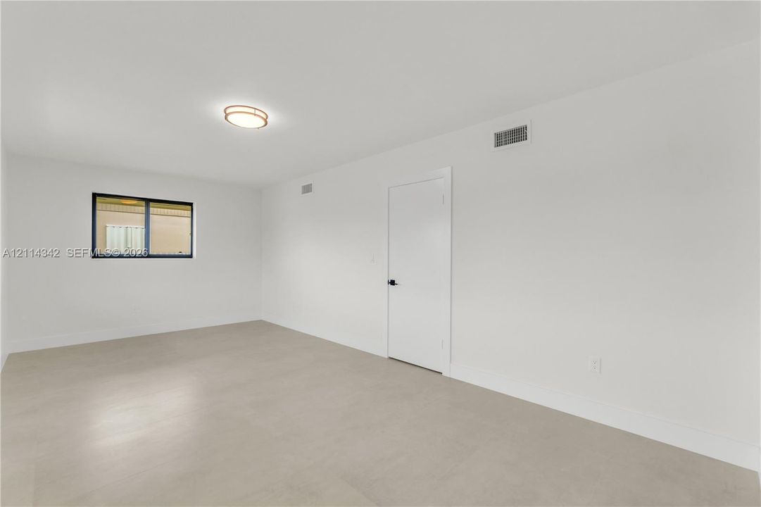 Neutral interior space featuring light-toned flooring, a single window with a black frame, and a circular flush-mount ceiling light fixture