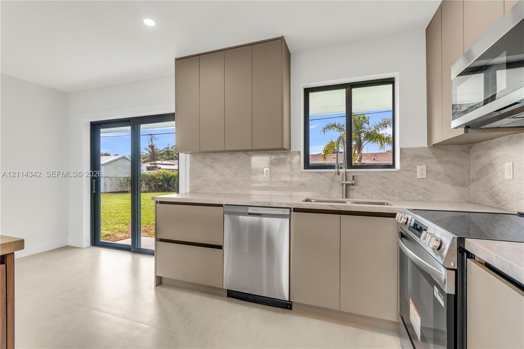 Kitchen featuring flat-panel cabinetry, full-height stone-finish backsplash, stainless steel appliances, and large-format tile flooring with access to the exterior via sliding glass doors
