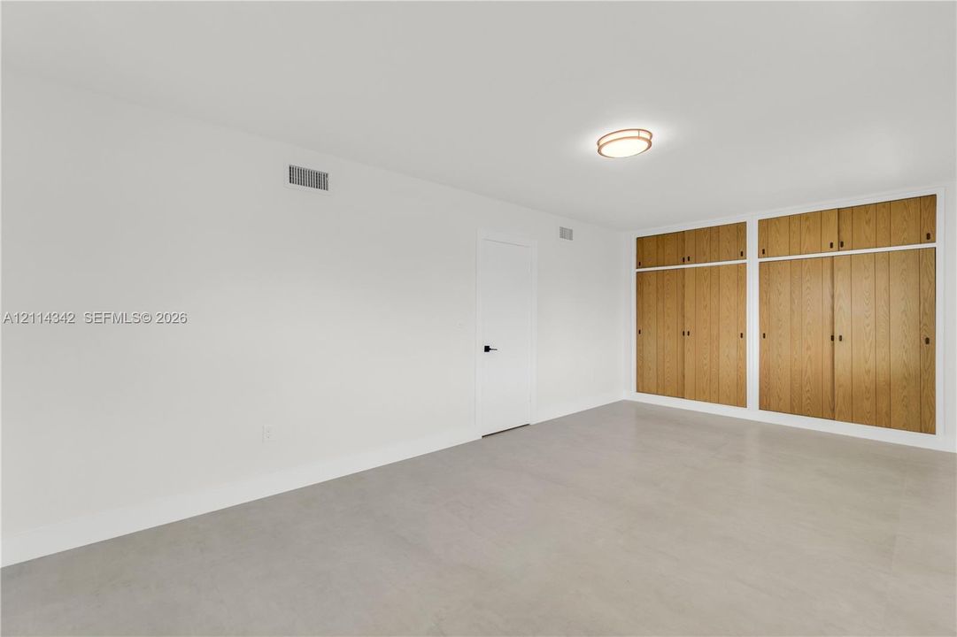 Neutral-toned flooring, expansive wall-to-wall built-in wood cabinetry, and a flush-mount circular ceiling fixture
