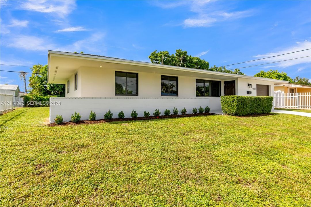Mid-century modern exterior featuring a low-slope roof, crisp white stucco finish, recessed soffit lighting, and manicured foundation plantings