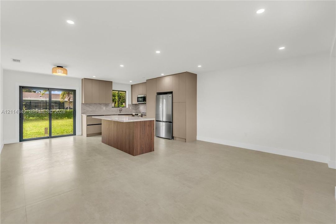 Open-concept kitchen featuring flat-panel cabinetry, a central island with stone-finish countertops, stainless steel appliances, recessed lighting, and sliding glass doors