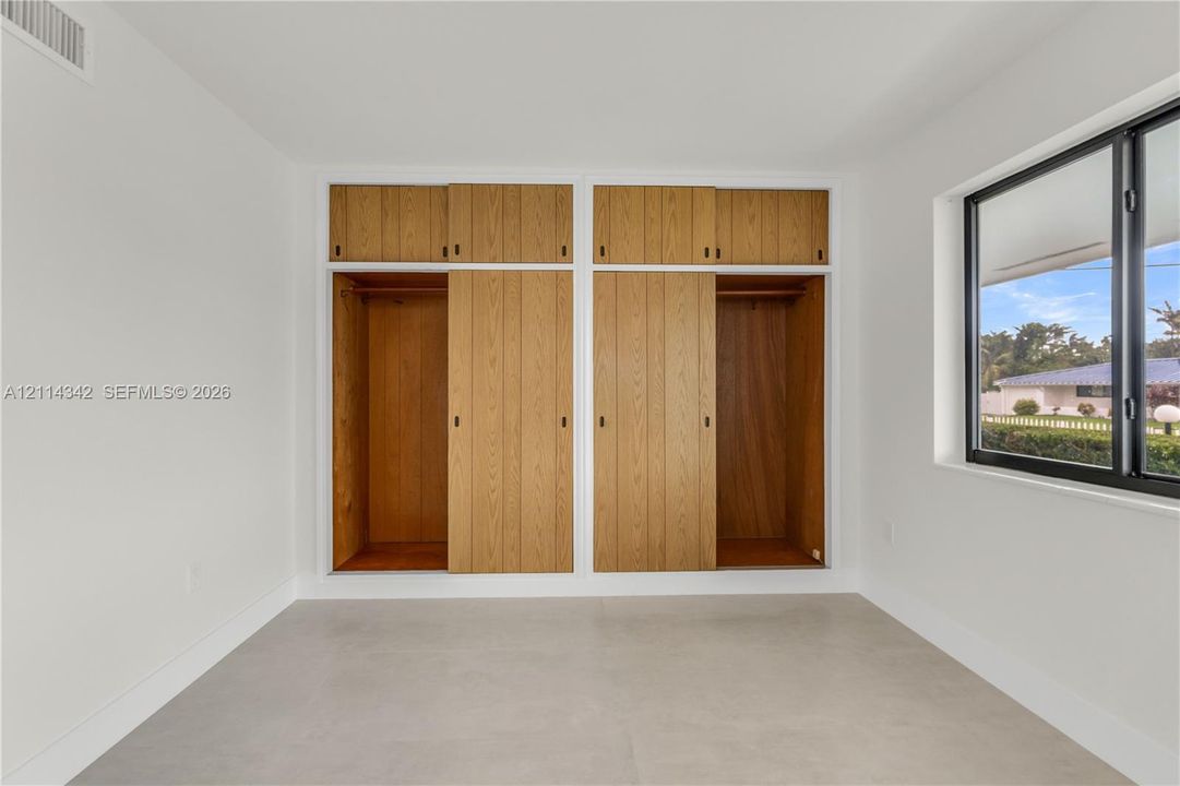 Built-in wooden cabinetry with sliding doors, neutral tile flooring, and large window with black framing