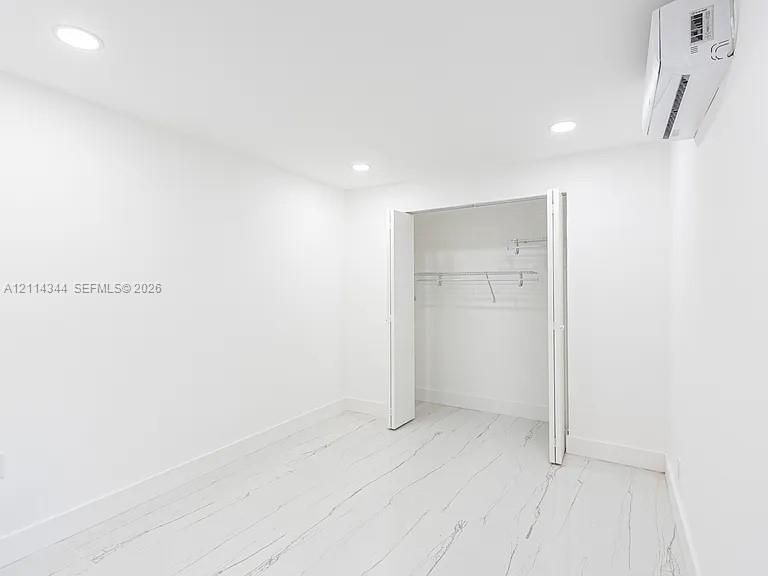 Interior room featuring stone-finish flooring, recessed lighting, a wall-mounted climate control unit, and a closet with bifold doors