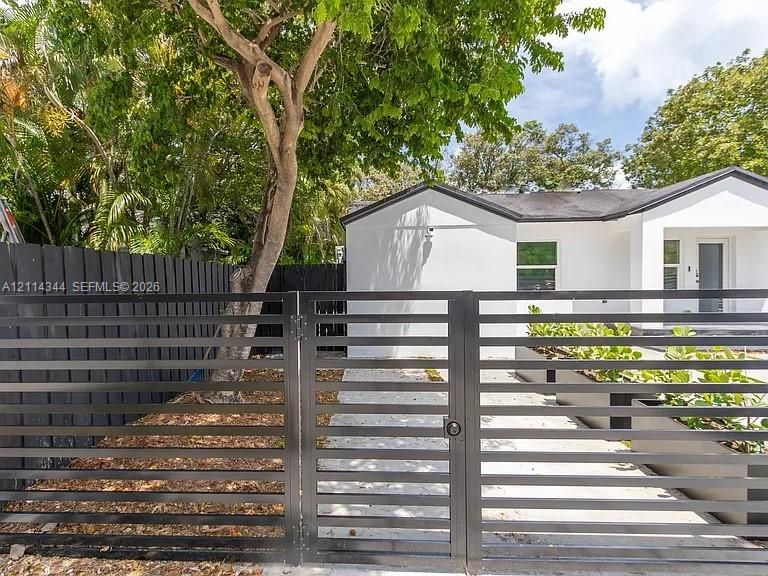Modern exterior with white stucco facade, matte black horizontal slat fencing, a matching swing gate, and concrete paver walkway