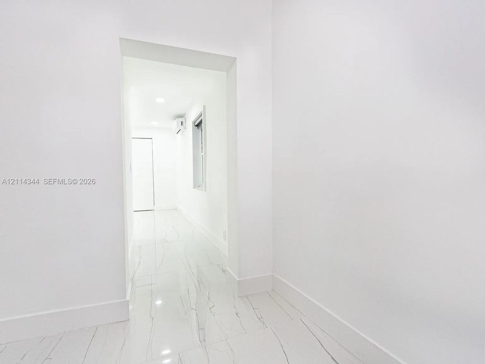 Minimalist interior featuring large-format stone-finish flooring with veining, smooth white walls, recessed ceiling lighting, and a wall-mounted climate control unit