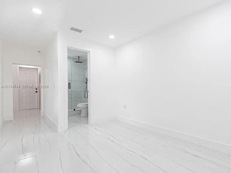 Polished stone-look flooring, recessed ceiling lighting, and a glass-enclosed shower with a rainfall showerhead