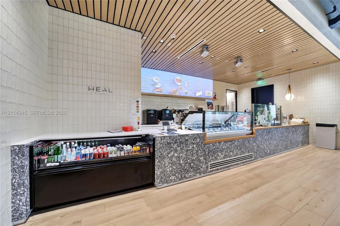 Custom service counter featuring patterned composite stone facing, wood-slat ceiling detail, white square tile wall cladding, wood-finish flooring, and recessed lighting