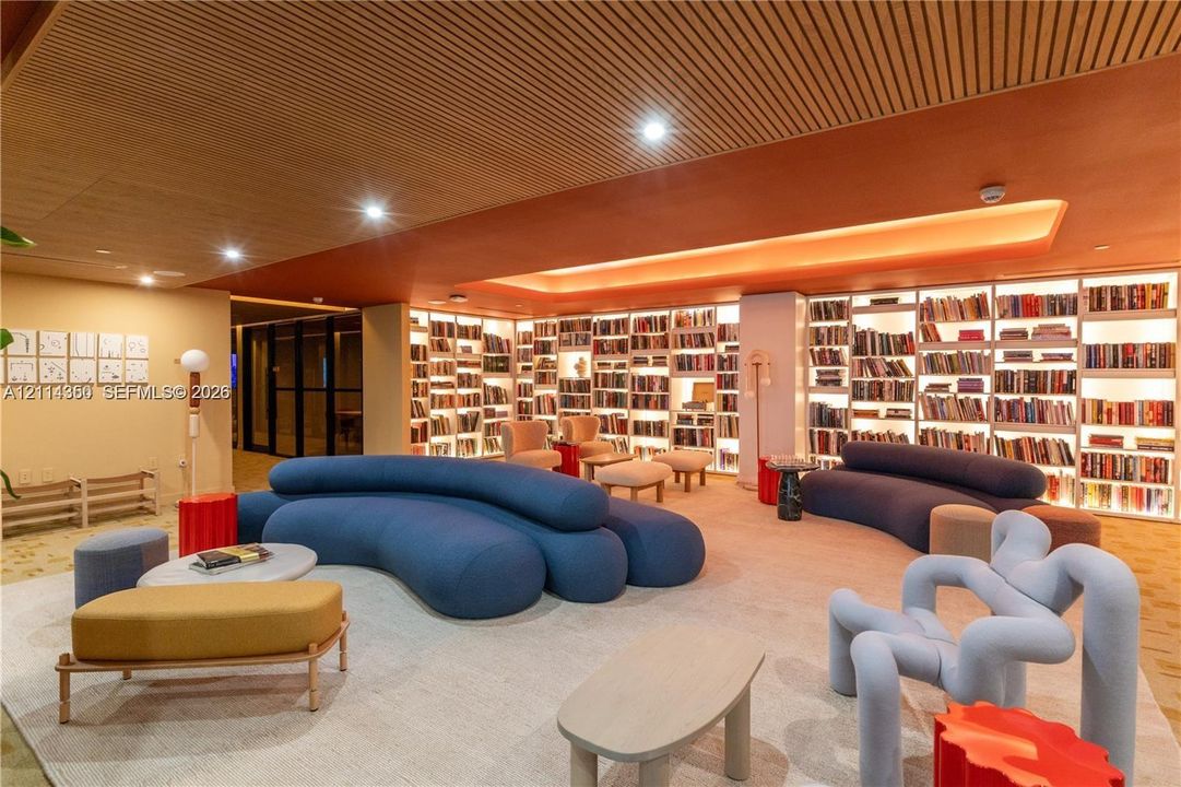 Expansive room featuring floor-to-ceiling built-in library shelving with integrated lighting, a slatted wood ceiling, recessed ceiling lighting, and a cove ceiling with accent illumination