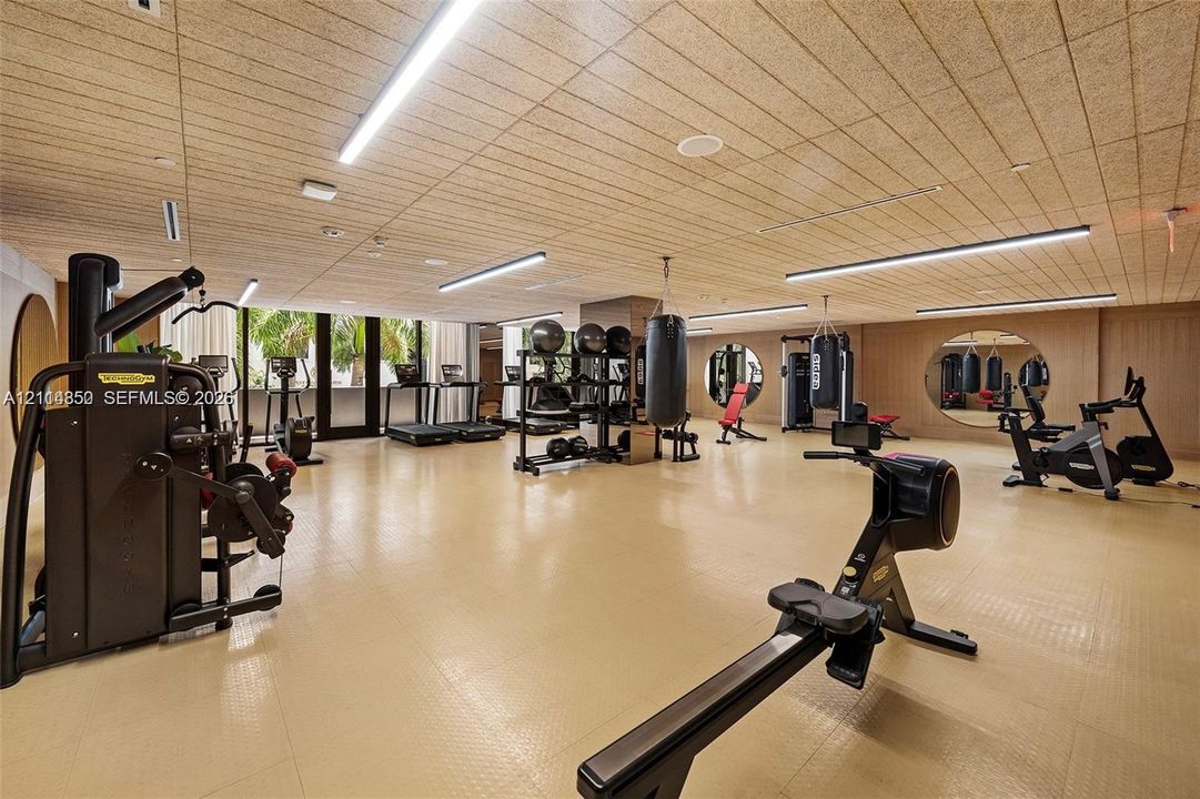 Fitness area featuring a textured ceiling finish, linear LED lighting, circular wall mirrors, and rubberized athletic flooring