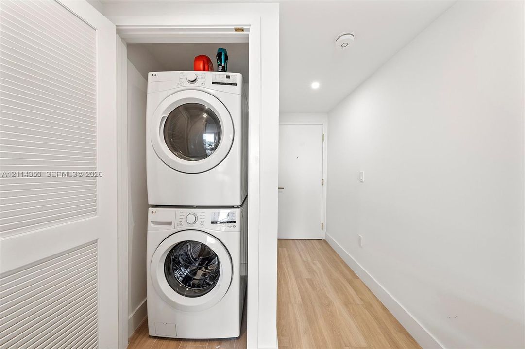 Laundry closet featuring a stacked white front-load washer and dryer, louvered door, recessed lighting, and wood-finish flooring