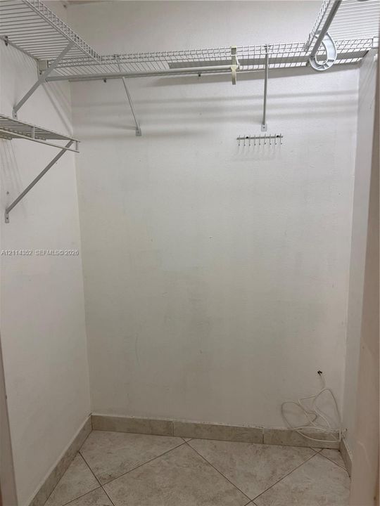 Storage space featuring light-toned tile flooring and wall-mounted wire shelving with integrated garment rods