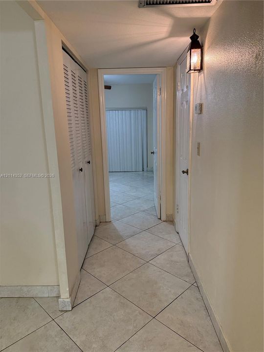 Hallway featuring neutral-toned tile flooring, dual-door closet with louvered panels, solid-core interior doors, and wall-mounted carriage-style lighting