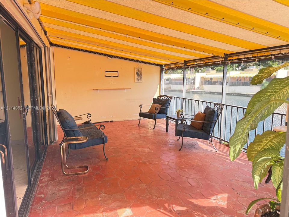 Covered patio featuring red stone-style flooring, a striped retractable awning, a metal railing, and direct water access