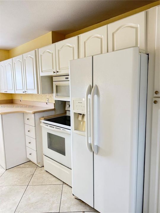 Kitchen featuring white cabinetry with arched panel detailing, integrated white appliances, solid-surface countertops, and diagonal tile flooring