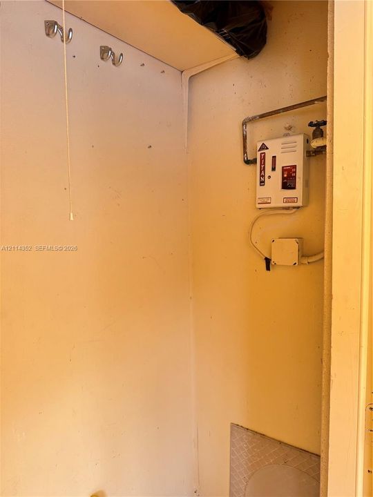 Tankless electric water heater featuring mounted metal wall hooks and an upper storage shelf