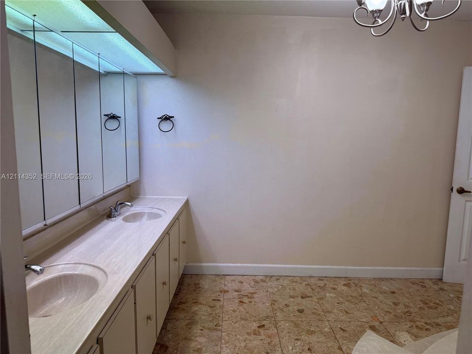Dual-sink vanity with integrated countertop and full-width mirror, featuring a recessed lighting soffit and terrazzo-style flooring