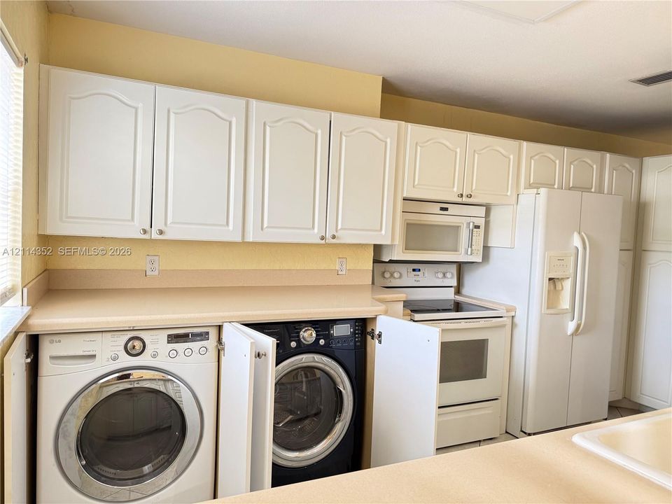 Kitchen featuring white cabinetry, integrated laundry appliances, solid-surface countertops, and a white refrigerator with built-in water and ice dispenser