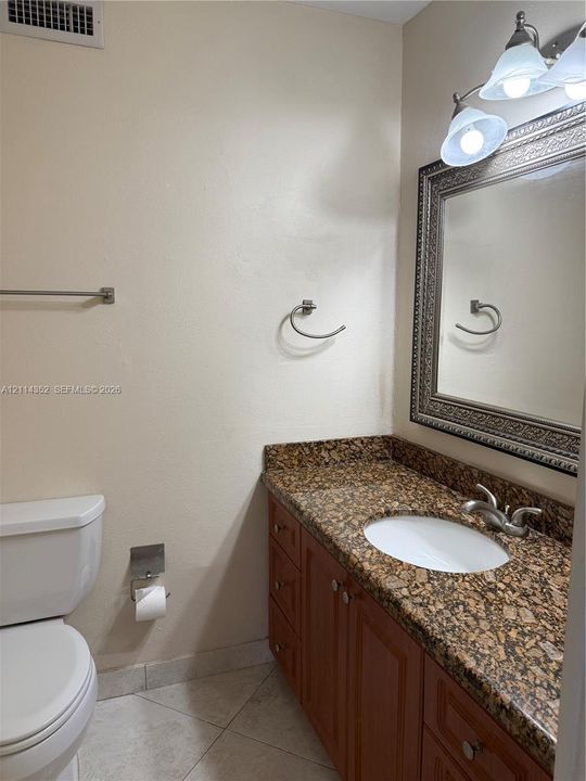 Bathroom vanity featuring a stone-surface countertop, an oval undermount sink, multi-drawer wood-finish cabinetry, a decorative framed mirror, and a three-light vanity fixture