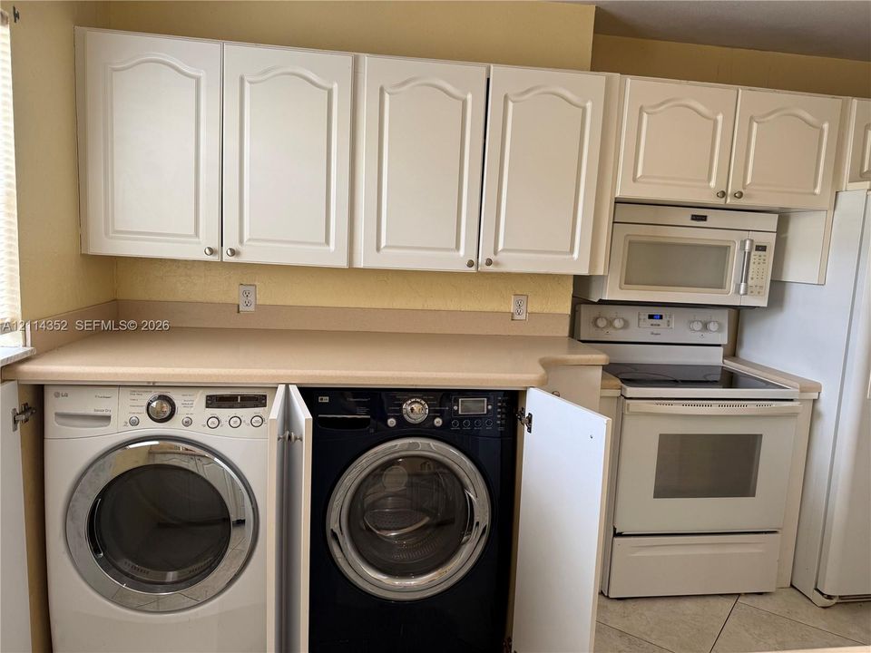 Built-in white cabinetry, solid-surface countertop, over-the-range microwave, electric range, and integrated laundry appliances